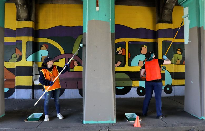 Volunteers Kaylynn Burke, left, and Rowan Finkle work to restore the extensive Aurora Bridge Mural by Patrick Gabriel from 1996 during the Seattle Day of Service. About a dozen joined the effort  under the north end of the Aurora Bridge on North 38th Street. The Fremont Arts Council organized this Day of Service effort to refresh the work on the northern retaining wall of the Highway 99/Aurora Avenue underpass at North 38th Street. (Alan Berner / The Seattle Times)