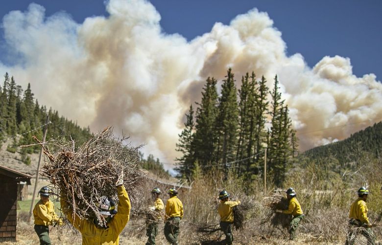 Firefighters with Structure Group 4 clear brush and debris away from cabins along Highway 518 near the Taos County line in New Mexico, May 13, 2022, while fire rages over the nearby ridge. (Jim Weber/Santa Fe New Mexican via AP) NMSAN302 NMSAN302