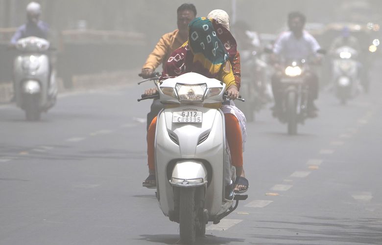 A woman covers her face with a scarf to protect from heat wave rides through a dust storm in Ahmedabad, India, Saturday, May 21, 2022. The intense heat wave sweeping through South Asia was made more likely due to climate change and it is a sign of things to come. An analysis by international scientists said that this heat wave was made 30-times more likely because of climate change, and future warming would make heat waves more common and hotter in the future. (AP Photo/Ajit Solanki) IHW101 IHW101