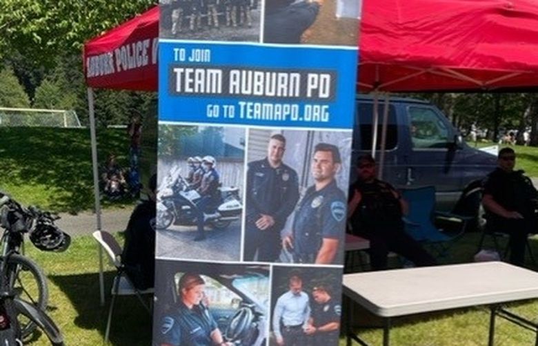 This banner was displayed at an Auburn Police Department recruiting booth on Saturday, May 21, 2022, at Game Farm Park, 3030 R Street SE, as part of the city’s “Pet Palooza” celebration. Officer Jeff Nelson, pictured in the center-right image below the text with his hands clasped in front of his waist, is awaiting trial in King County Superior Court on charges of second-degree murder and first-degree assault in the May 31, 2019, shooting death of Jesse Sarey. He is currently on paid leave pending the trial, which likely will occur next spring. (Photo courtesy of Jeff Trimble)