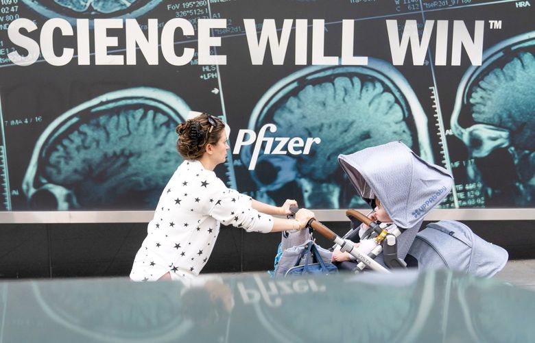 A woman pushes a baby in a stroller past a sign hanging outside Pfizer headquarters in New York, Monday, May 23, 2022. Three doses of Pfizer’s COVID-19 vaccine offer strong protection for children younger than 5, the company announced Monday, May 23, 2022. Pfizer plans to give the data to U.S. regulators later this week in a step toward letting the littlest kids get the shots. (AP Photo/Mary Altaffer) NYMA106
