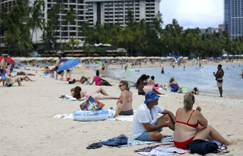 Brett Walsh and Emma Yates, bottom right, tourists from Australia, sit on Waikiki Beach in Honolulu, Monday, May 23, 2022. A COVID surge is under way that is starting to cause disruptions as schools wrap up for the year and Americans prepare for summer vacations. Case counts are as high as they’ve been since mid-February and those figures are likely a major undercount because of unreported home tests and asymptomatic infections. But the beaches beckoned and visitors have flocked to Hawaii, especially in recent months. (AP Photo/Caleb Jones) HICJ206 HICJ206