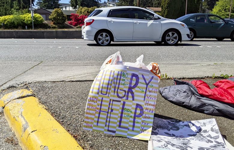 “Hungry, help,” reads a sign by Brad Peterson, 51, who advertises that he is looking for work on Highway 99 in Edmonds, Snohomish County, Friday, May 20, 2022. Peterson went to school at Edmonds College and later worked in construction, but said an injury has left him unable to work full-time.
