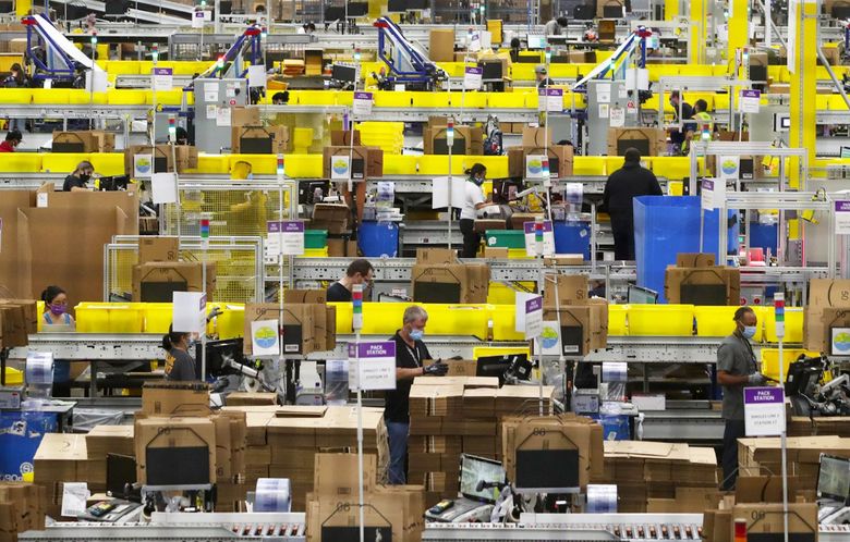 Employees work at packing stations at Amazon’s Kent fulfillment center in June 2020. Amazon shareholders approved a $212 million payout for CEO Andy Jassy Wednesday and voted against all 15 proposals introduced at the meeting. (Ken Lambert / The Seattle Times)