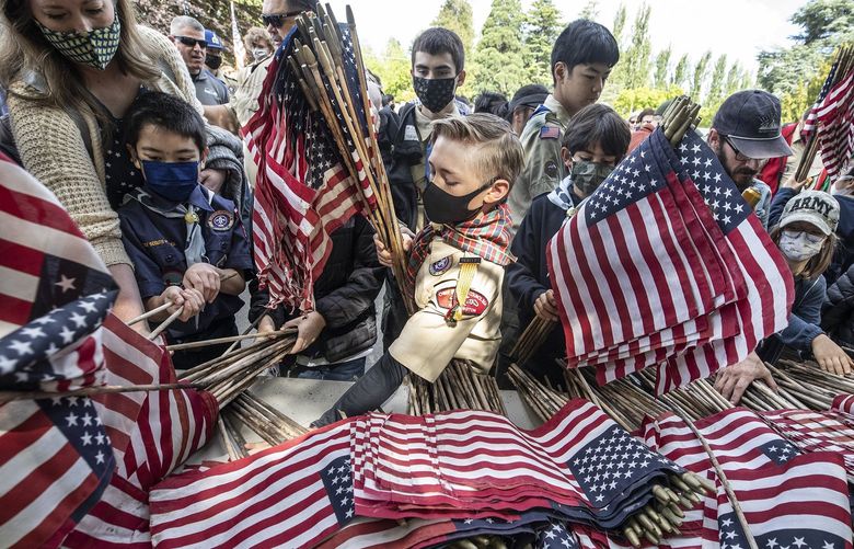 Monday, May 31, 2021. Lines Only. LO. Scouts rush the table to pick up ceremonial flags including Jared Petras, 10, at center, from Shorelines Pack 319 at the 95th Annual Memorial Day at Washelli Memorial Cemetery. Each of the 5,000 white upright marble markers received a flag placed by scouts, community members and veterans. 217282