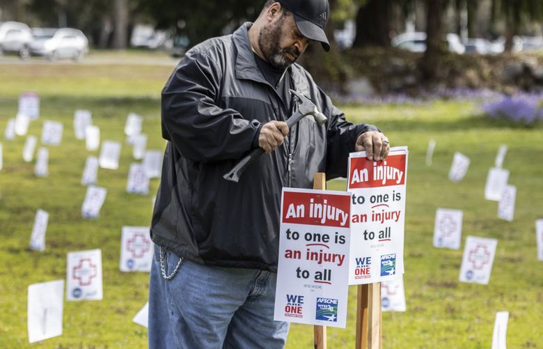 Thursday, April 28, 2022.    John Henson, a medical escort worker drives placards on the grounds of Western State Hospital surrounded by another 400 symbolizing the number of assulted workers injured at the hospital in the last calender year.  The Washington Federation of State Employees union local 793 organized the rally on Worker Memorial Day, calling attention to those who have been injured.    220254