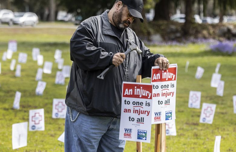 Thursday, April 28, 2022. John Henson, a medical escort worker drives placards on the grounds of Western State Hospital surrounded by another 400 symbolizing the number of assulted workers injured at the hospital in the last calender year. The Washington Federation of State Employees union local 793 organized the rally on Worker Memorial Day, calling attention to those who have been injured. 220254