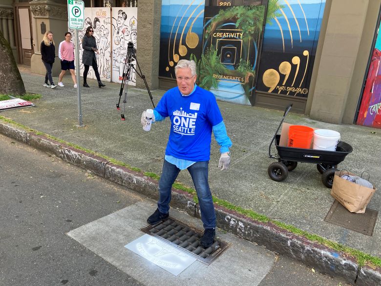Seahawks Coach Pete Carroll uses a stencil and spray paint to mark on a First Avenue South drain: “Drains to Salish Sea. Dump no waste.” Carroll and about 400,000 other volunteers were taking part in One Seattle Day of Service activities on Saturday. (Erik Lacitis / The Seattle Times)