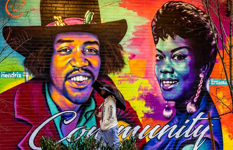 Jaerl Perry, of St. Louis, is visiting uses an umbrella as he passes public art painted on the Midtown Square building as it rains. Local Seattle artist Myron Curry painted a few murals on 23rd Avenue honoring the images of past leaders according to the Midtown Square website. The murals honor past figures like Jimi Hendrix, Ernestine Anderson, DeCharlene Williams, Langston Hughs and Edwin T. Pratt.