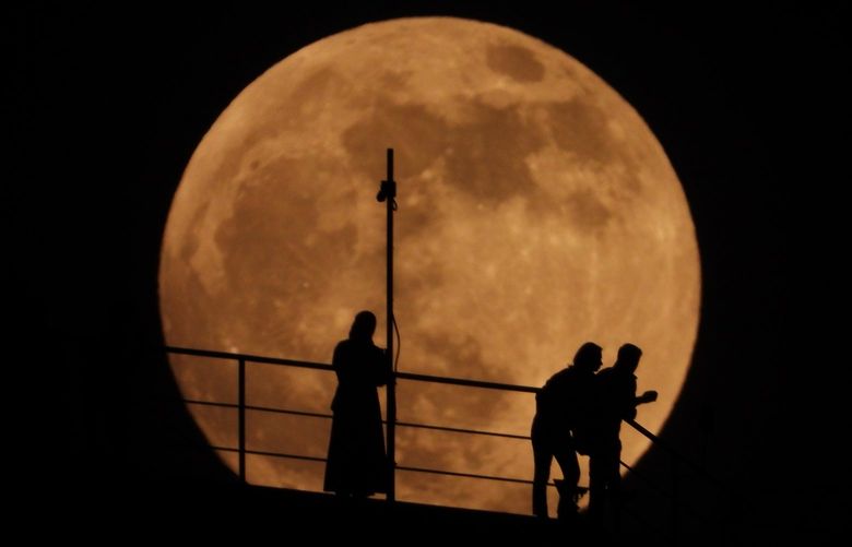 People are silhouetted as an almost full moon rises above the sky in Grozny, Russia, Sunday, May 15, 2022. (AP Photo/Musa Sadulayev) LUN109 LUN109