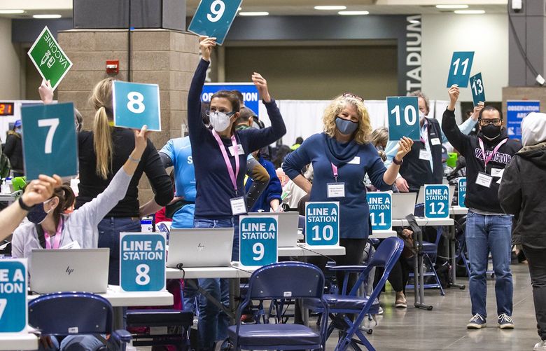 Volunteers at vaccination stations raise their numbers to show they are available for the next person in line at the new Community Vaccination Site at Lumen Field Event Center in Seattle Saturday March 13, 2021. The site was opened to a limited number of people to start, but has estimated capacity to vaccinate up to 22,000 people per day if supplies are available, which could make it the largest civilian-run vaccination site in the country. 216644