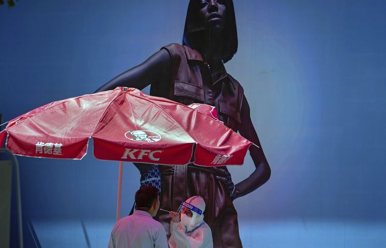 A medical worker in protective suit collects a sample from a resident at a COVID test site setup in front of a fashion billboard on Wednesday, May 18, 2022, in Beijing. (AP Photo/Andy Wong) XAW101 XAW101