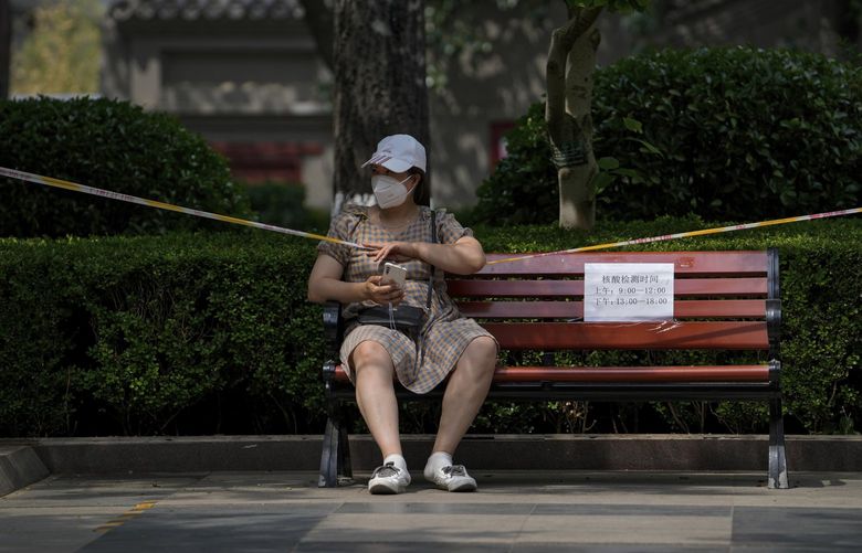 A woman wearing a face mask sits on a barricaded bench in a park to prevent residents gathering due to pandemic measures Monday, May 23, 2022, in Beijing. Beijing extended orders for workers and students to stay home and ordered additional mass testing Monday as cases of COVID-19 again rose in the Chinese capital. (AP Photo/Andy Wong) XAW102 XAW102