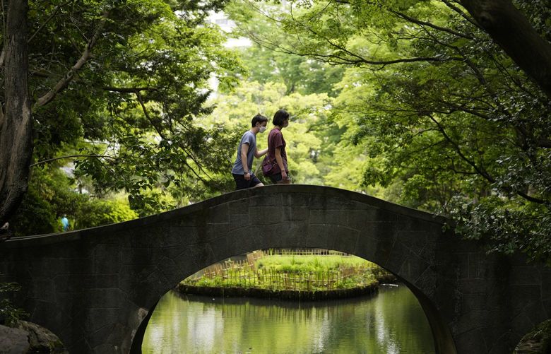 People wearing face masks walk cross a small bridge over a pond at a park in Tokyo, Thursday, May 19, 2022. (AP Photo/Hiro Komae) TKHK207 TKHK207