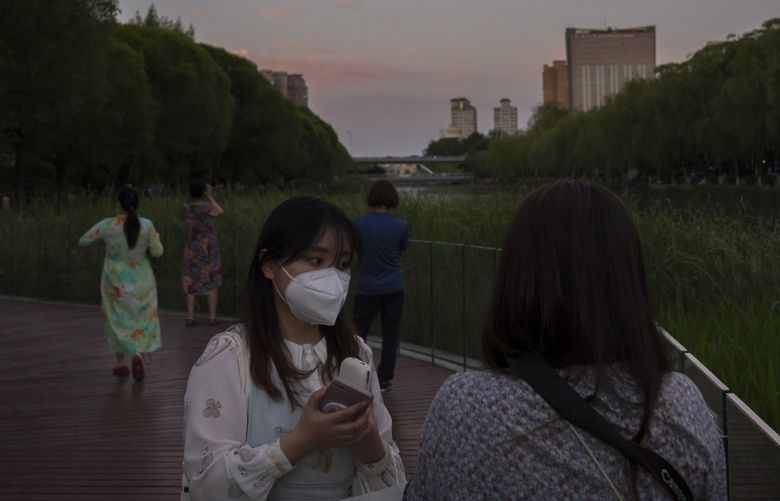 A woman wearing a face mask stands in a green space along a waterway at sunset in Beijing, Thursday, May 26, 2022. (AP Photo/Mark Schiefelbein) XMAS105 XMAS105