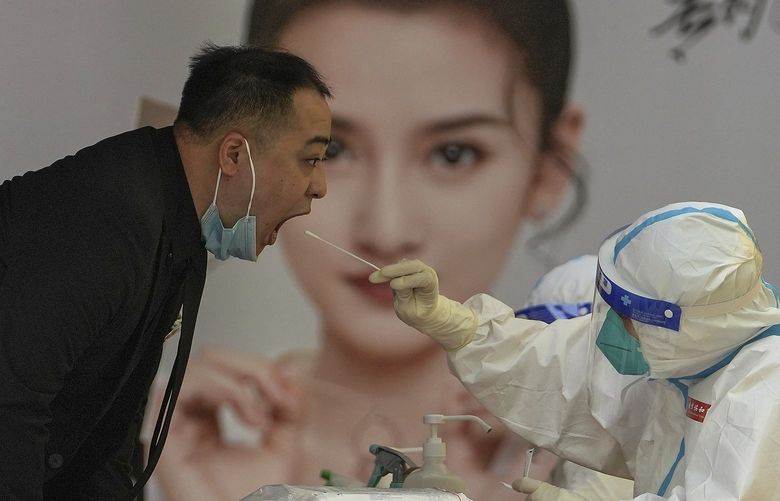A medical worker in protective gear collects a sample from a worker at a COVID testing site setup outside a shopping mall on Sunday, May 22, 2022, in Beijing. (AP Photo/Andy Wong) XAW102 XAW102