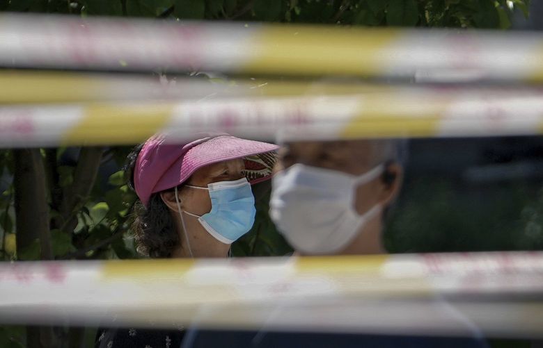 Residents wearing face masks line up behind barricaded tapes for COVID mass testing near a residential area on Sunday, May 15, 2022, in Beijing. (AP Photo/Andy Wong) XAW101 XAW101