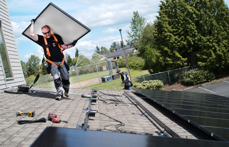 Lenne Edwardson, an employee of MAD Energy, seen left, installs a solar panel at Kent United Methodist Church, May 11, 2022 in Kent, Wash. The solar panels installed atop Kent United Methodist Church is a community project made possible through a $102,000 grant from Puget Sound Energy.