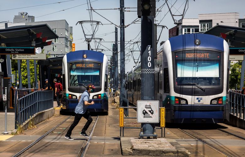 A man dashes in front of an oncoming southbound light-rail train, stopped to unload passengers, to catch a northbound train, at right, at the south end of the Othello station, Tuesday, June 7, 2022 in Seattle. The trains run along Martin Luther King, Jr. Way South.