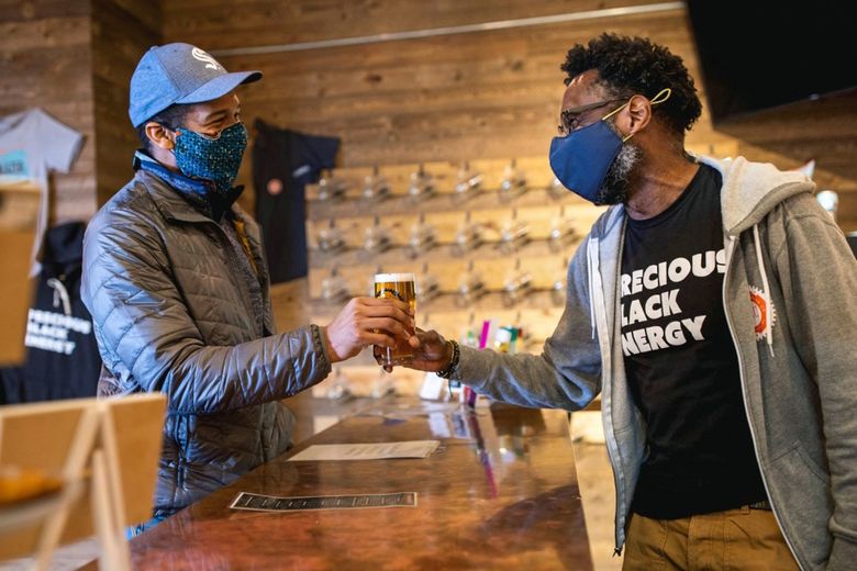 Rodney Hines, co-owner of Métier Brewing Co., right, hands a pint to Roland Remolana, left, in his Woodinville taproom. Métier recently opened a new taproom in the Central District. (Photo courtesy of William Muñoz)