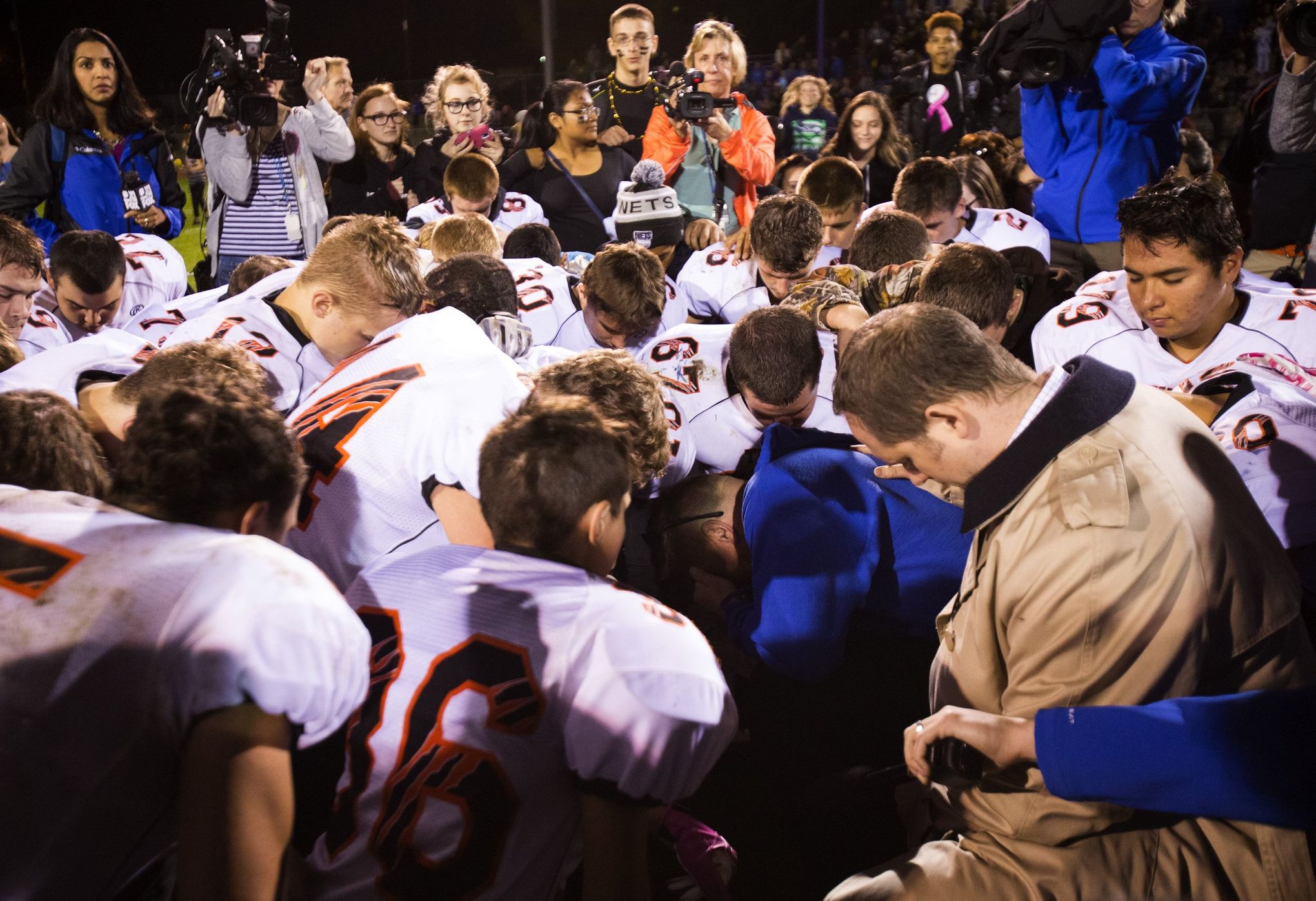 Kennedy kneeling in prayer surrounded by high school football players