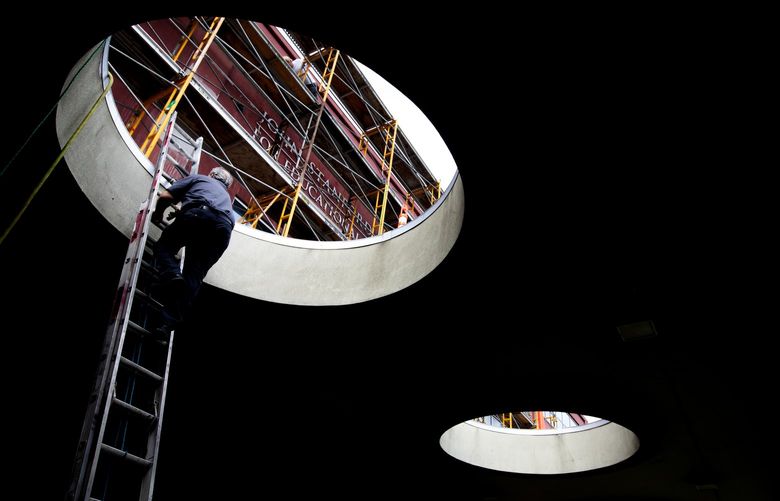 Seen through one of the holes that are part of the architecture of the John Stanford Center for Educational Excellence, where Seattle Public Schools (SPS) is headquartered, SPS maintenance worker Brian Almquist goes up a ladder during repairs to the facade, Wednesday, June 22, 2022 in Seattle’s SODO neighborhood. Almquist is part of a team making repairs that, according to SPS spokesman Tim Robinson, includes concrete work in advance of painting this one area. According to an email from Robinson, “It’s an isolated fix-up, not part of a larger renovation. Our facilities team does a fantastic job keeping all our buildings in tip-top shape.” The 1950’s era building that used to be a U.S. Postal Service hub is included on a list with 106 schools in the district that are monitored for maintenance, according to Robinson.