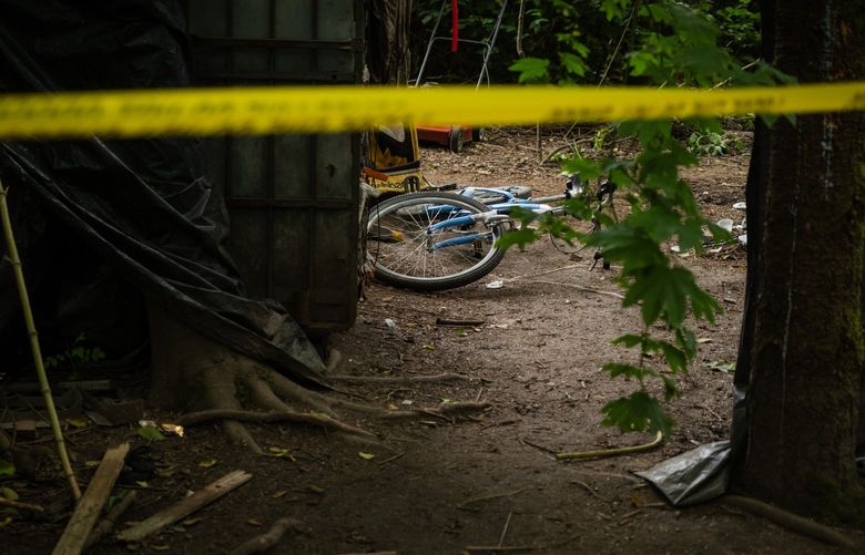 A blue bicycle rests on the ground behind caution tape at a homeless encampment in West Seattle after police said a person was shot and killed there on June 20, 2022.