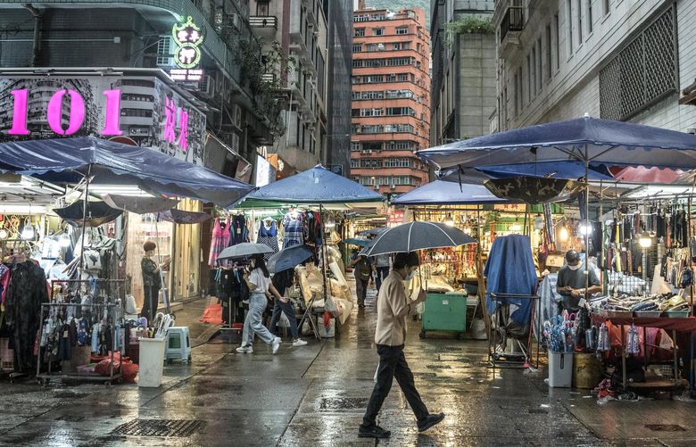 People walk through shops on Queen’s Road in Hong Kong, June 8, 2022. There was a time when many Hong Kong youth felt proud of their dual identity: Chinese, yes, but a special kind who cherished British common law and custardy egg tarts with Portuguese provenance. (Sergey Ponomarev/The New York Times)