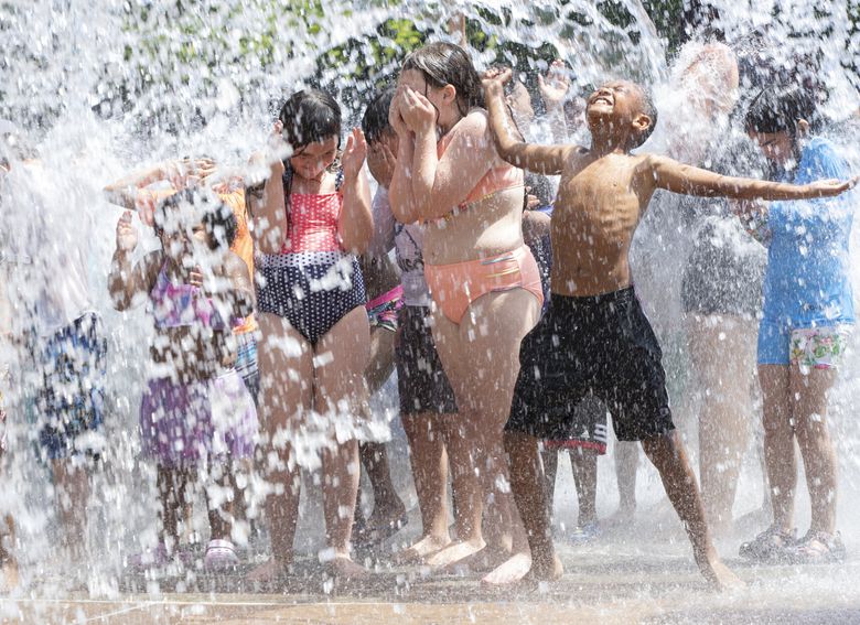 A group of children celebrates as water jets out of the ground at the Angle Lake Spray Park in SeaTac on June 27, 2022, when temperatures peaked at 91degrees. The hot weather isn’t expected to last with highs only estimated to reach 68 degrees on Tuesday and similar weather expected throughout the rest of the week. (Ellen M. Banner / The Seattle Times)