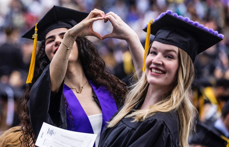 Lindsay Harmon and friend Maha Fathali send a heart to family and friends during commencement at Husky Stadium at the University of Washington in Seattle on June 11, 2022. (Daniel Kim / The Seattle Times)