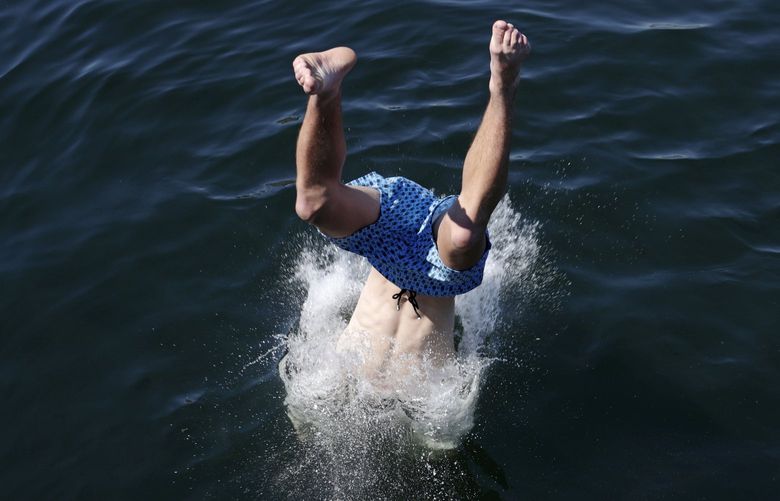 A person dives into the water from a pedestrian bridge at Lake Union Park into the water during a heat wave hitting the Pacific Northwest, Sunday, June 27, 2021, in Seattle. Yesterday set a record high for the day with more record highs expected today and Monday. (AP Photo/John Froschauer)