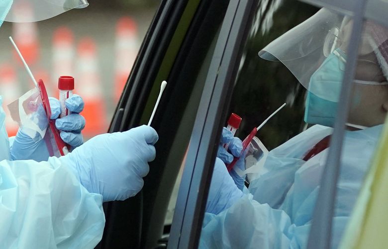 Linsey Jones, a medical assistant working at a drive-up COVID-19 testing clinic, hands a nose swab to a person in a car, Tuesday, Jan. 4, 2022, in Puyallup, Wash., south of Seattle. People using the facility, which is being run by the Pierce County Dept. of Emergency Management, faced waits of several hours Tuesday for testing. (AP Photo/Ted S. Warren) WATW111