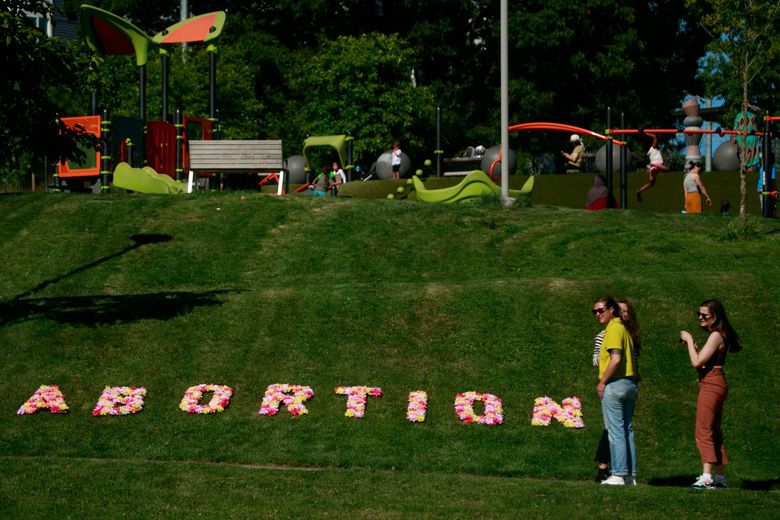 Kirsten Ohlendorf, wearing green, and Chloe Alexander, wearing brown, help place an abortion sign during the Shout Your Abortion gathering to protest the Supreme Court decision overturning Roe v. Wade at Yesler Terrace Park in Seattle on June 24, 2022. Shout Your Abortion, a national organization based in Seattle, provided materials to make signs, a station to thank abortion providers and provided information materials. (Erika Schultz / The Seattle Times)