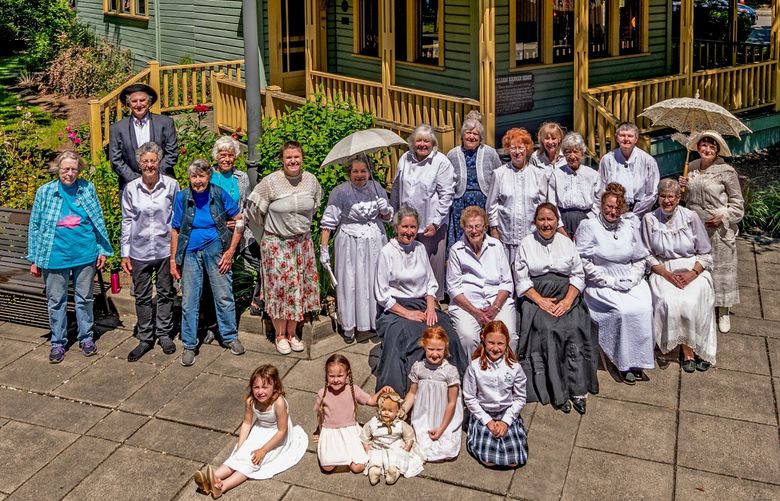 NOW1: Repeating the pose at the William Hannan home, now situated at Bothell Landing and housing the Bothell Historical Museum (BothellHistoricalMuseum.org), are 18 women, four girls and a man, including several descendants of historical city figures. For names of those pictured, visit PaulDorpat.com. Credit: Jean Sherrard

NOW1 (with full identifications, for possible online use): Repeating the pose at the William Hannan home, now situated at Bothell Landing and housing the Bothell Historical Museum (BothellHistoricalMuseum.org), are 18 women, four girls and a man, including several descendants of historical city figures. Complete identifications follow. Standing, back left: Bill Carlyon, great-grandson of Bothell pioneers William and Jemima Hannon and grandson of Gladys Hannan Worley, their daughter, who was born and married in the parlor. Standing, from left: Pat Pierce, Jill Keeney, Jeanette Backstrom, Sue Kienast, Melanie Carlyon McCracken (daughter of Bill and Emmy Carlyon and great, great granddaughter of the Hannans), Pippin Sardo, Emmy Carlyon (wife of Bill Carlyon), Margaret Turcott, JoAnne Hunt, Linda Avery, Margaret Carroll, Mary Evans and Pamela McCrae. Seated, from left: Terry Roth, Iva Metz, Carol King, Nancy Velando and Mary Anne Gibbons. Children in front, from left: Wendy Stow (Linda Avery’s granddaughter) and Camille, Evelyn and Mira McCracken (great, great, great granddaughters of the Hannans).