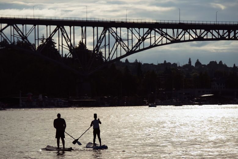 Paddleboarders head toward the Aurora Bridge on Monday before it grew dark enough for the Lake Union fireworks display. (Amanda Ray / The Seattle Times)