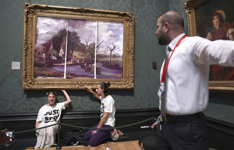 A security guard looks at protesters who glued their hands to the frame of John Constable’s The Hay Wain, inside the National Gallery, London, Monday July 4, 2022. Police say two climate change protesters have been arrested after they glued themselves to the frame of a famous John Constable painting hanging in Britainâ€™s National Gallery. The two, from the protest group â€œJust Stop Oil,â€ stepped over a rope barrier and covered â€œThe Hay Wainâ€ on Monday with large sheets of paper depicting â€œan apocalyptic vision of the futureâ€ of the landscape. (Kirsty O’Connor/PA via AP) AMB822 AMB822