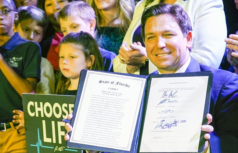 FILE – Florida Gov. Ron DeSantis holds up a 15-week abortion ban law after signing it on April 14, 2022, in Kissimmee, Fla. Reproductive health providers sued Florida on Wednesday, June 1, 2022, alleging that the law violates a provision in the state constitution guaranteeing a person’s right to privacy, “including the right to abortion.” (AP Photo/John Raoux, File) NYAB305