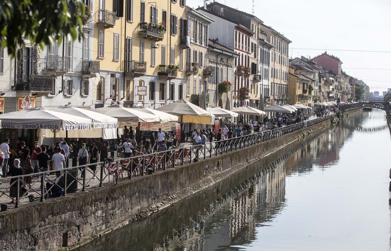 FILE – People walk along the Naviglio Grande canal in Milan, Italy on May 24, 2020. Travel to Europe might be an attractive option to travelers looking for a budget vacation in 2022. The dollar is strong this year, meaning your cash can go further on the continent. (AP Photo/Luca Bruno, File) 