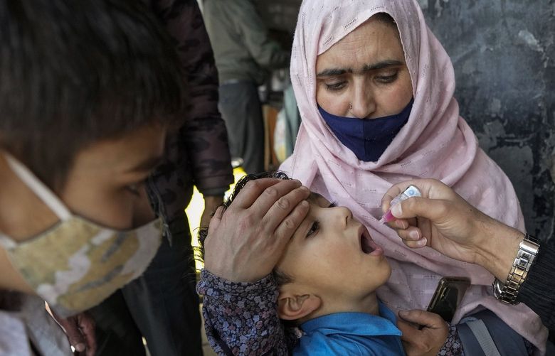 A medical volunteer administers a dose of polio vaccine to a child as another watches at a bus station in Jammu, India, Sunday, Feb.27, 2022. Polio is a highly infectious disease that spreads in contaminated water or food and usually strikes children under 5. (AP Photo/Channi Anand)