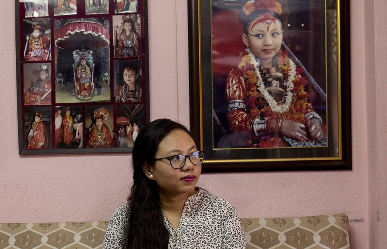 Chanira Bajracharya, 27, with pictures of her wearing her divine regalia, at her home in Kathmandu, Nepal, on June 25, 2022. Bajracharya was once a kumari, a young girl worshiped in Nepal as the embodiment of a Hindu goddess. (Uma Bista/The New York Times)