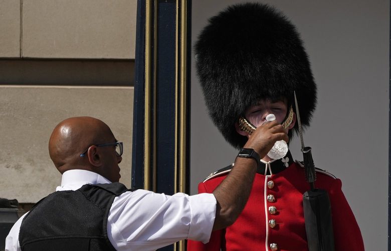 A police officer givers water to a British soldier wearing a traditional bearskin hat, on guard duty outside Buckingham Palace, during hot weather in London, Monday, July 18, 2022. The British government have issued their first-ever “red” warning for extreme heat. The alert covers large parts of England on Monday and Tuesday, when temperatures may reach 40 degrees Celsius (104 Fahrenheit) for the first time, posing a risk of serious illness and even death among healthy people, the U.K. Met Office, the country’s weather service, said Friday. (AP Photo/Matt Dunham)