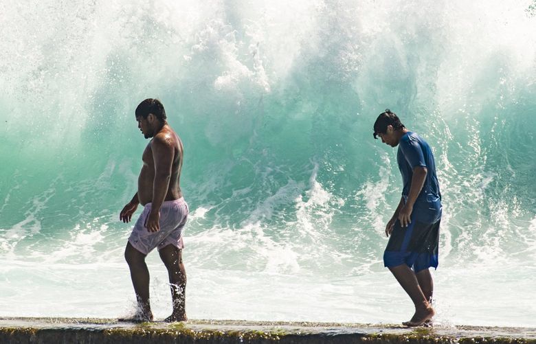 People walk in front of the high surf near Kapahulu Groin (Waikiki Wall) in Waikiki, Hawaii, Sunday, July 17, 2022. (Craig T. Kojima/Honolulu Star-Advertiser via AP) HIHON201 HIHON201
