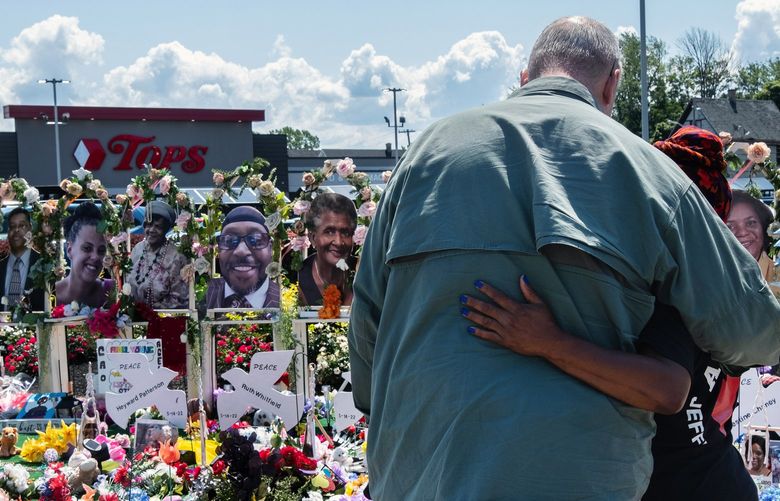 Two people embrace while viewing the sidewalk memorial outside Tops Friendly Market in Buffalo, N.Y., on Friday, July 15, 2022. The chain-link fencing was removed later on Friday for the public reopening of the store, where 10 people were slain in a white supremacist massacre on May 14. (Malik Rainey/The New York Times)