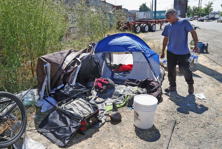 Man carries bottled water to his tent that was handed to him earlier by REACH outreach workers