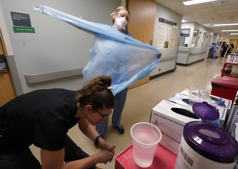 Registered nurse removes protective equipment and washes her hands after leaving a COVID-19 patient’s room