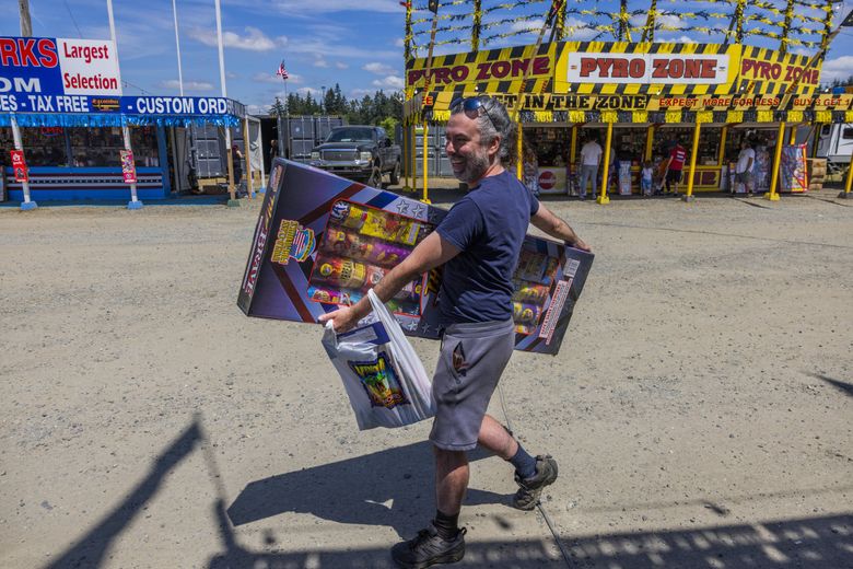 Phillip Kezele walks with his hands full of fireworks at the fireworks mall at the Muckleshoot Reservation last week. At about $170, Kezele said that he spent more than he wanted to on fireworks this year.  (Daniel Kim / The Seattle Times)