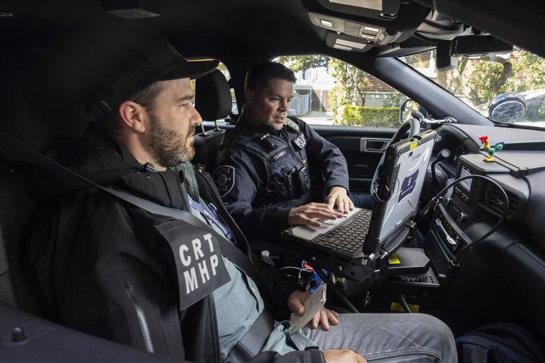 Responding to a repeated 911 calls from a man in distress, Seattle police crisis response team members Collin Jevmore, left, a mental health professional, and Officer Joe Binder look up the  man’s history before meeting with backup officers. (Steve Ringman / The Seattle Times)