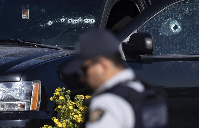 A police officer walks near a windshield and passenger window of an RCMP vehicle with bullet holes at the scene of a shooting in Langley, British Columbia, Monday, July 25, 2022. Canadian police reported multiple shootings of homeless people Monday in a Vancouver suburb and said a suspect was in custody. (Darryl Dyck/The Canadian Press via AP) VCRD108 VCRD108