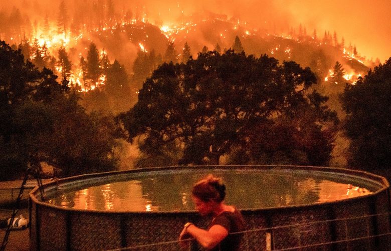 Angela Crawford leans against a fence as a wildfire called the McKinney fire burns a hillside above her home in Klamath National Forest, Calif., on Saturday, July 30, 2022. Crawford and her husband stayed, as other residents evacuated, to defend their home from the fire. (AP Photo/Noah Berger) CANB109