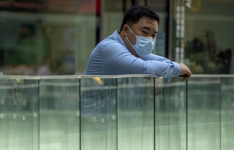 A man wearing a face mask looks over a railing at an office complex in Beijing, Thursday, Aug. 11, 2022. (AP Photo/Mark Schiefelbein) XMAS103 XMAS103